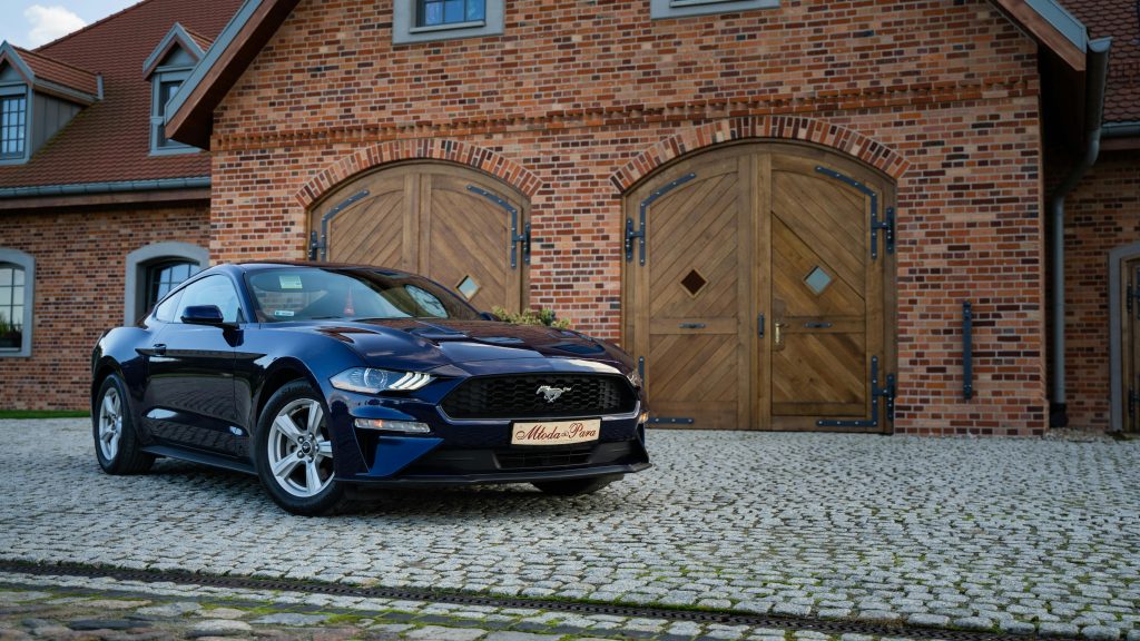 Sleek blue sports car parked outside a rustic brick building with wooden doors.